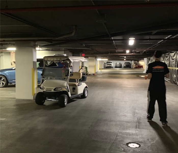 Inside a parking garage with a golf cart parked and a SERVPRO employee standing under the smoke damaged ceiling
