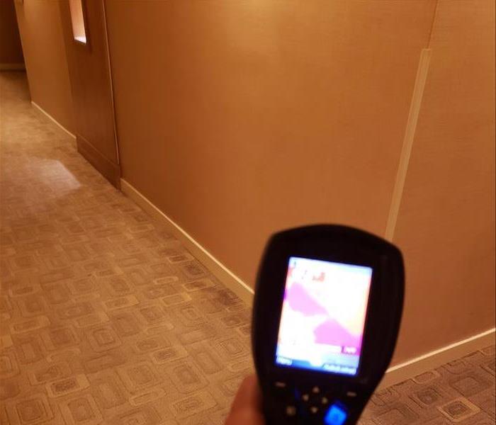 A hallway with water damage and a man holding a thermal moisture meter that is showing him the wet areas on its screen