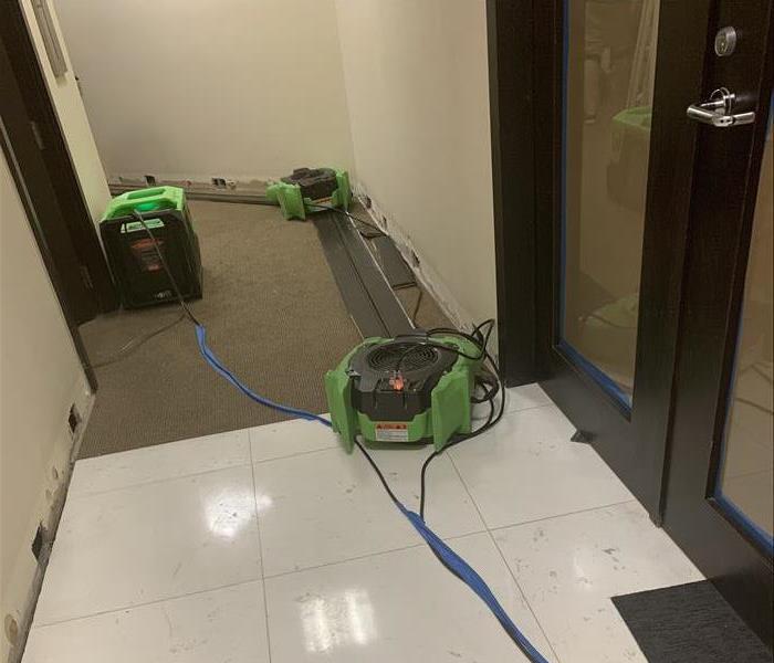 Office hallway with cream walls and dark carpets containing green air movers strategically placed for drying