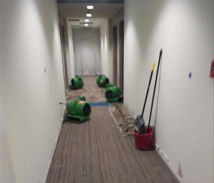 Hallway with partial carpet removed and drying equipment in place to dry the wet walls