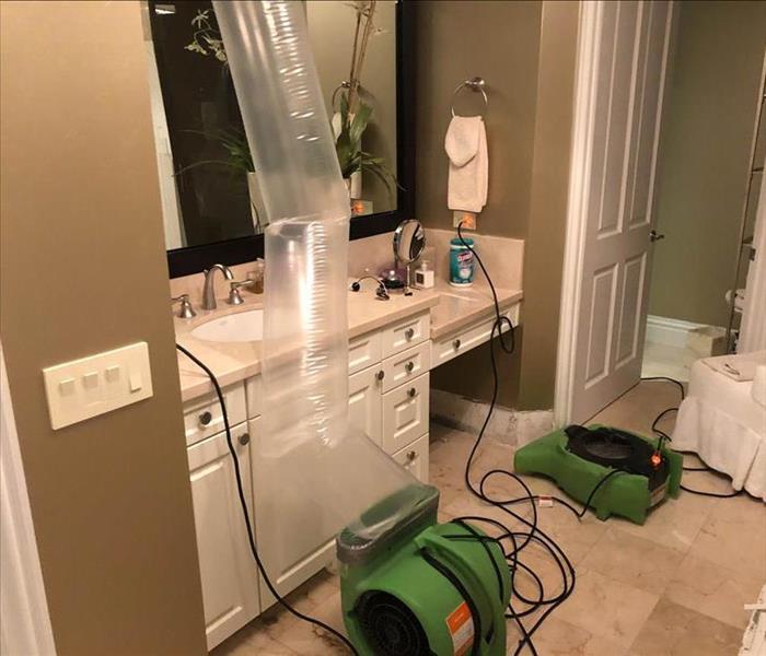 Bathroom with water damage and SERVPRO has set up air mover concentrating air flow to the damaged area