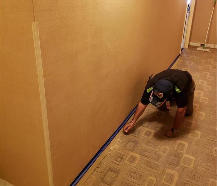 Man on knees cutting out damaged sheetrock in hallway